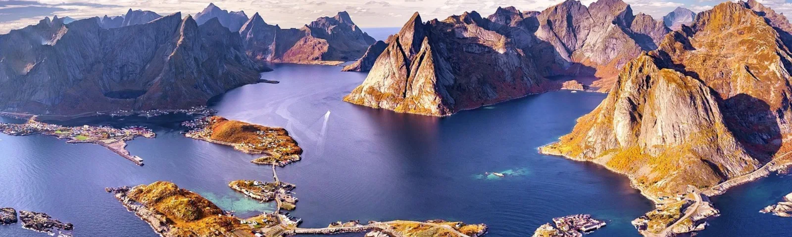Bilde av Reine i Lofoten sett fra luften. Bratte fjel, hav og blå himmel.