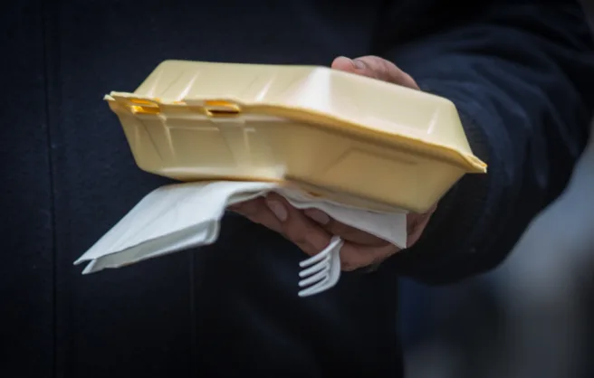 Hånd som holder plastbestikk og isoporbeholder til take-away.