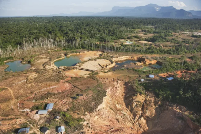 En gruve fremstår som et stort sår i landskapet. Rundt står skogen og viser tydelig hvilken natur som er rasert for grave.