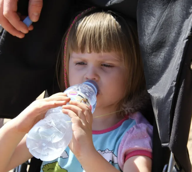 Liten jenten som drikker av en plastflaske.