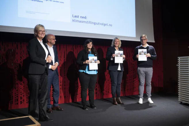 Bilde fra pressekonferansen, fem mennesker står på rekke på scenen med rapporten foran seg