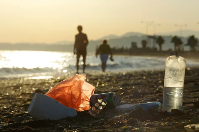 Plastforsøpling på stranden, siluetter av mennesker i bakgrunnen