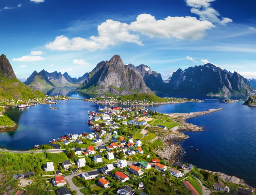 Sol, grønne trær, hus og fjell i Lofoten.